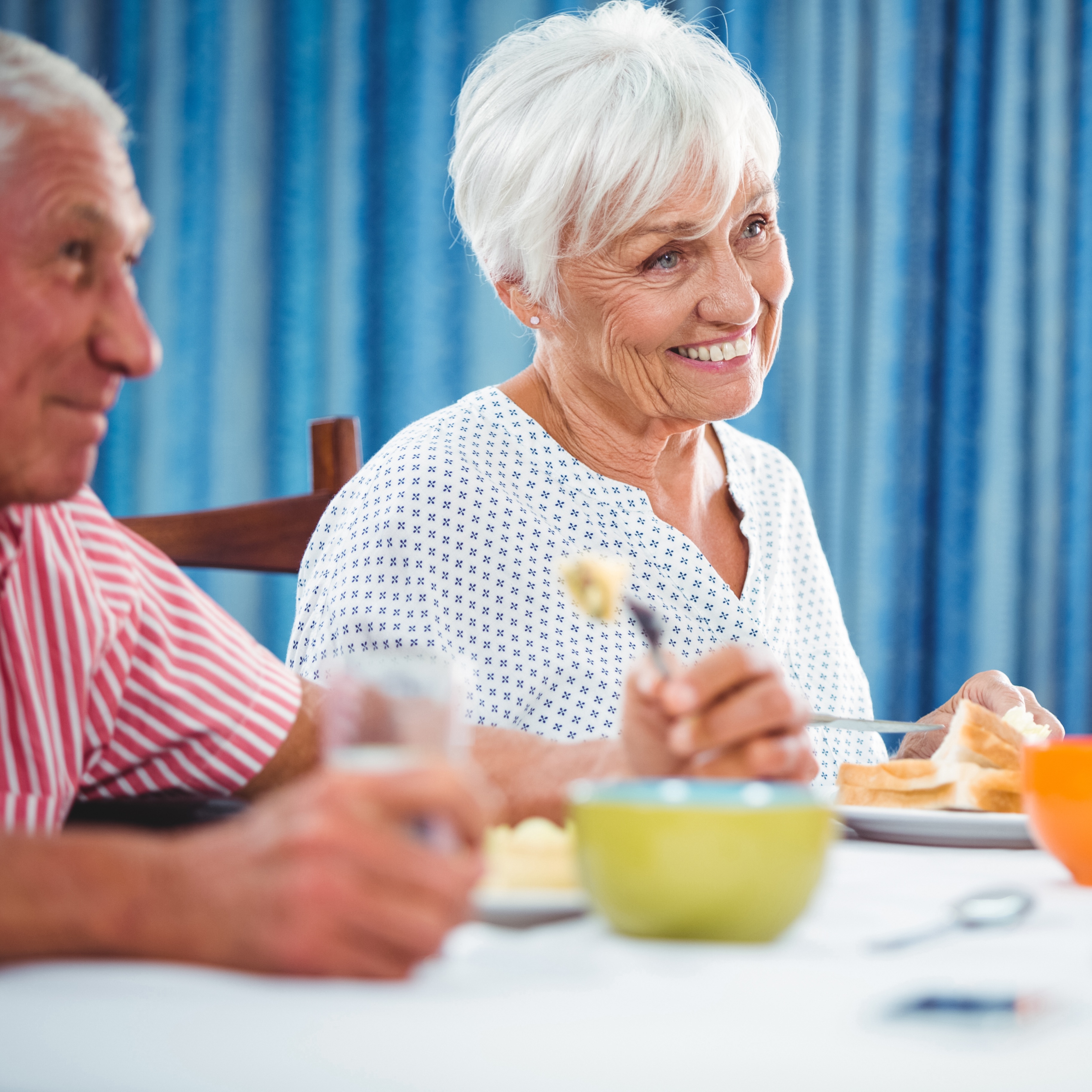 Lächelnde ältere Frau isst mit einem Mann an einem Tisch.
