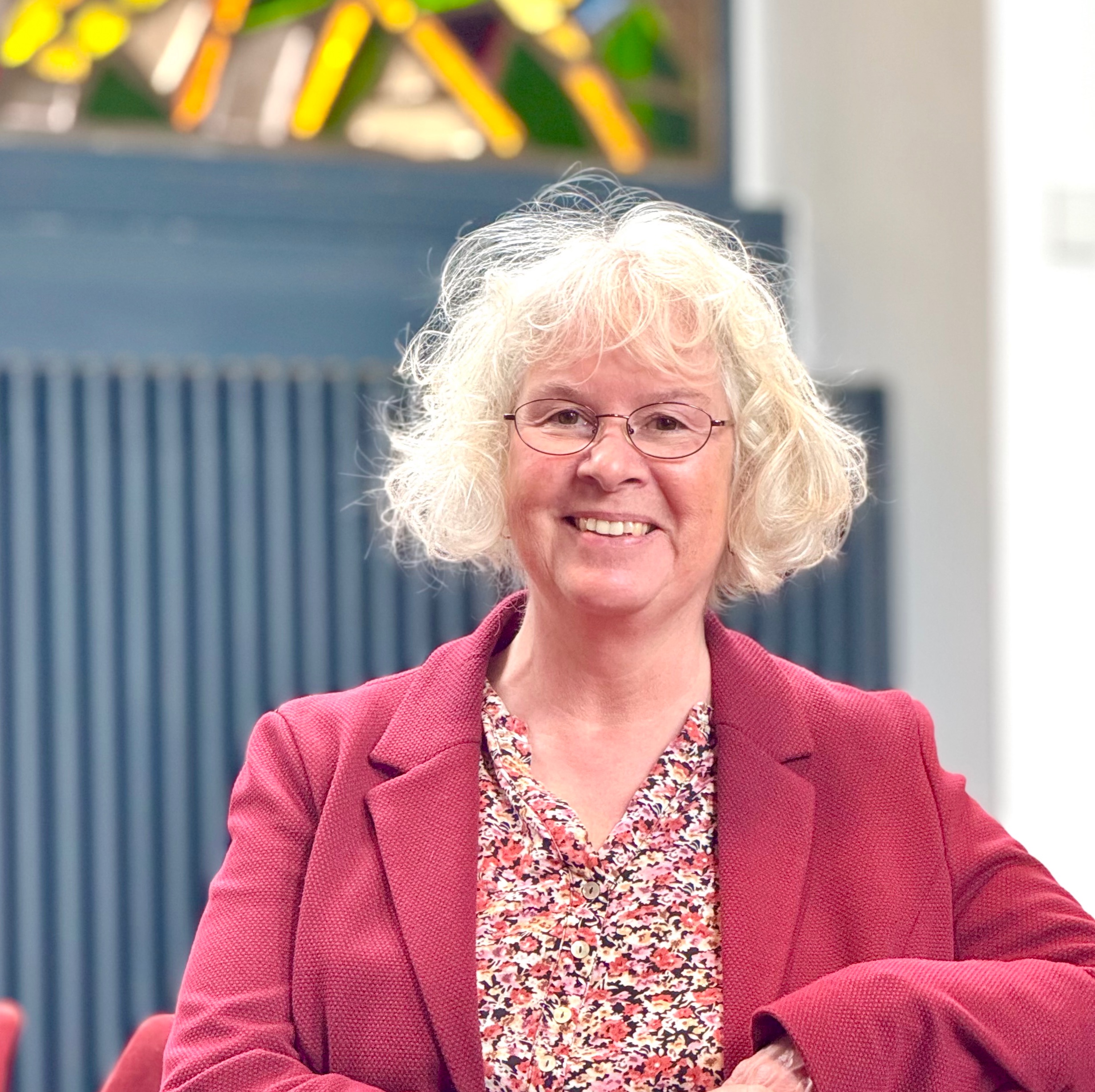 Lächelnde Frau mit Brille und weißen lockigen Haaren drinnen.