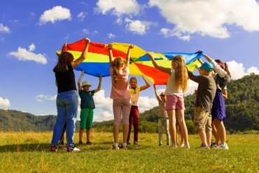 Gruppe Kinder hält einen bunten Fallschirm auf einem sonnigen Feld.