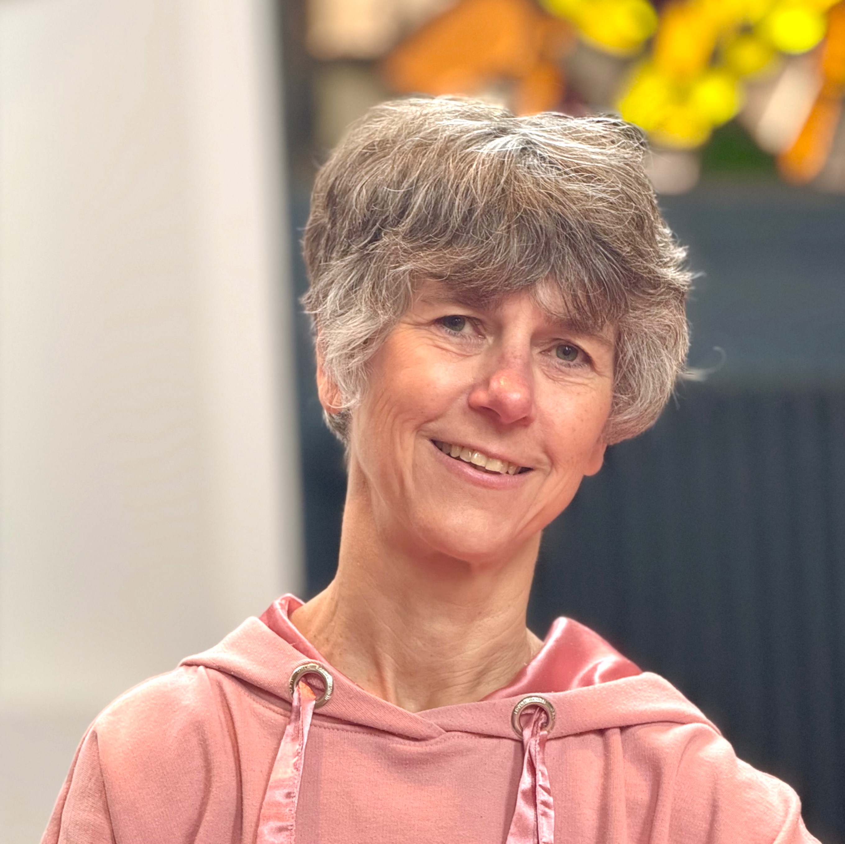 Lächelnde Frau mit kurzen grauen Haaren und pinkem Kapuzenpullover.