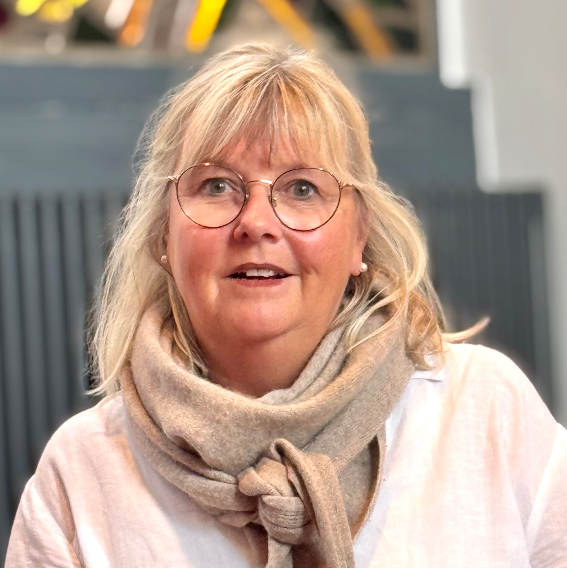 Lächelnde Frau mit blonden Haaren und runder Brille drinnen.