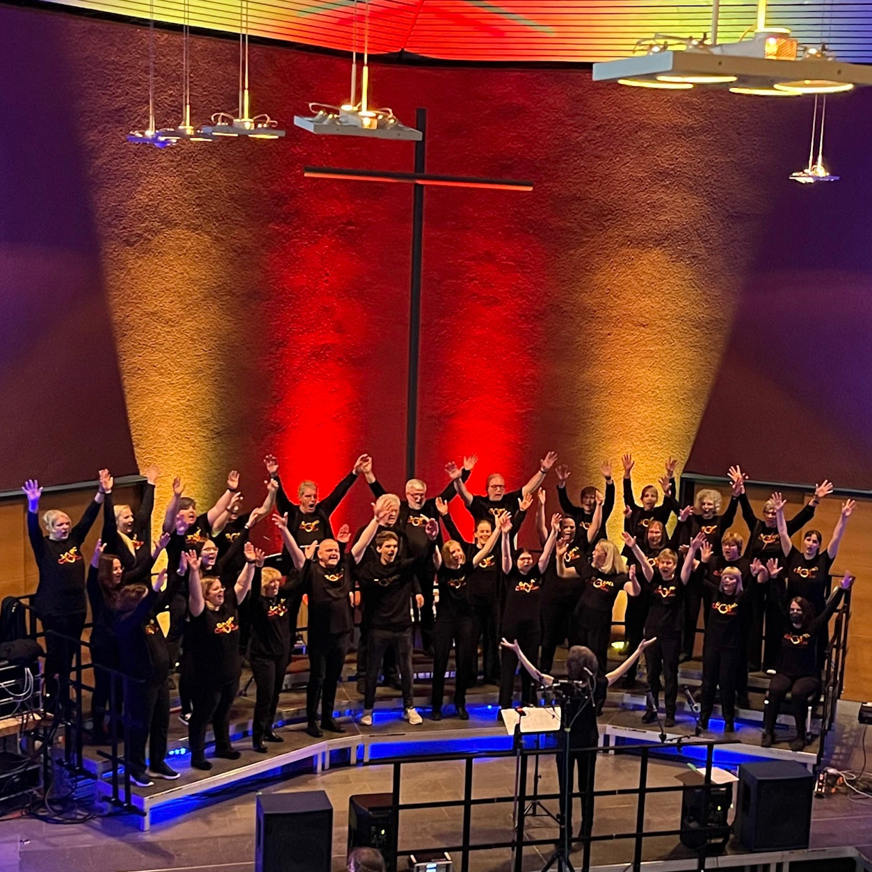 Großer Chor mit erhobenen Händen tritt auf einer Bühne mit Kreuz auf.