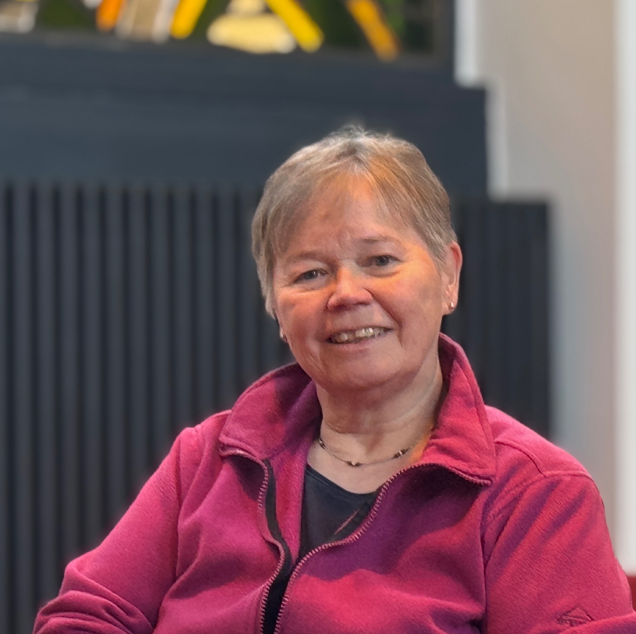 Lächelnde Frau mit kurzen blonden Haaren und Brille drinnen.