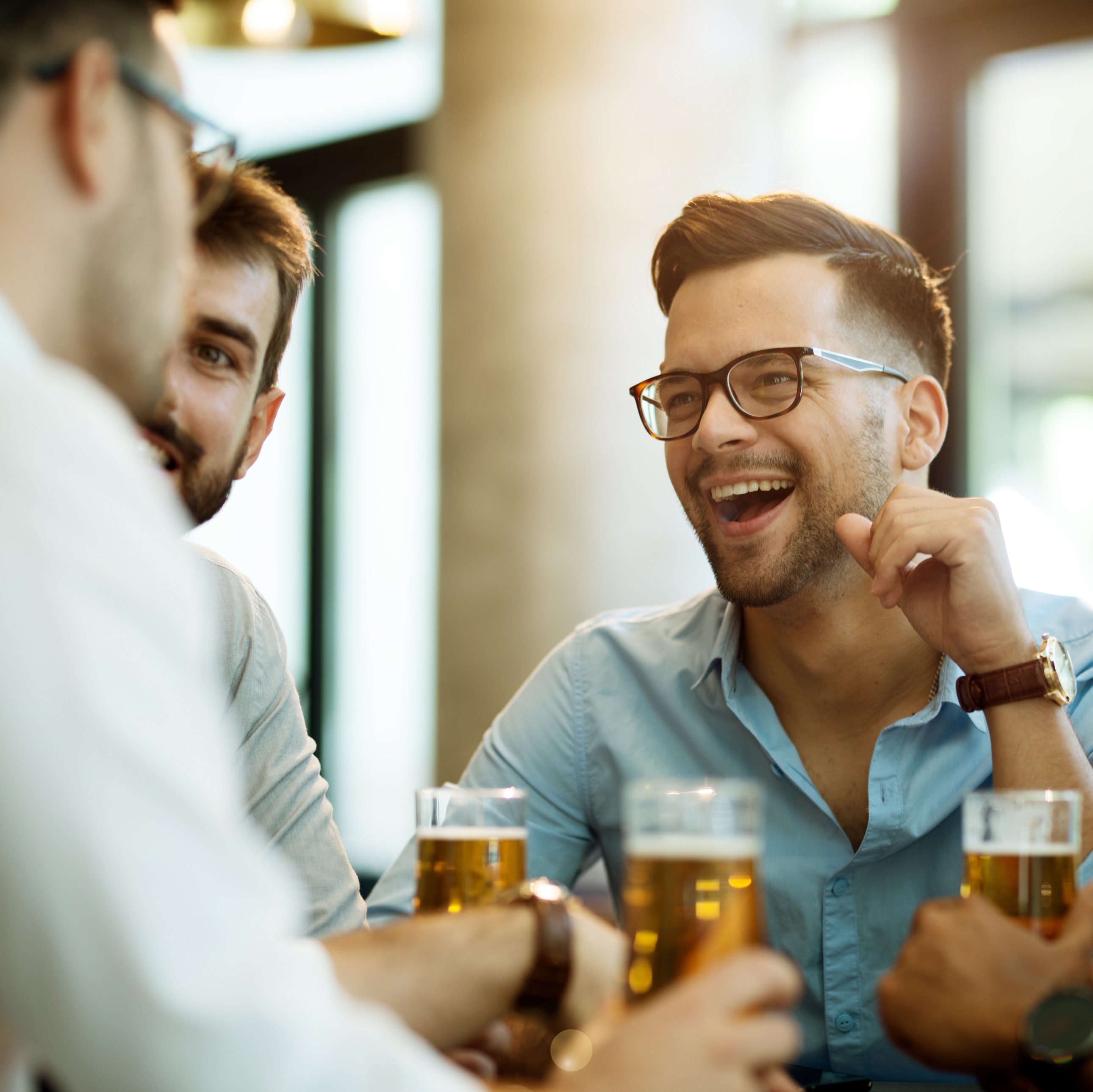 Drei junge Männer lachen und halten Bier an einem Tisch.