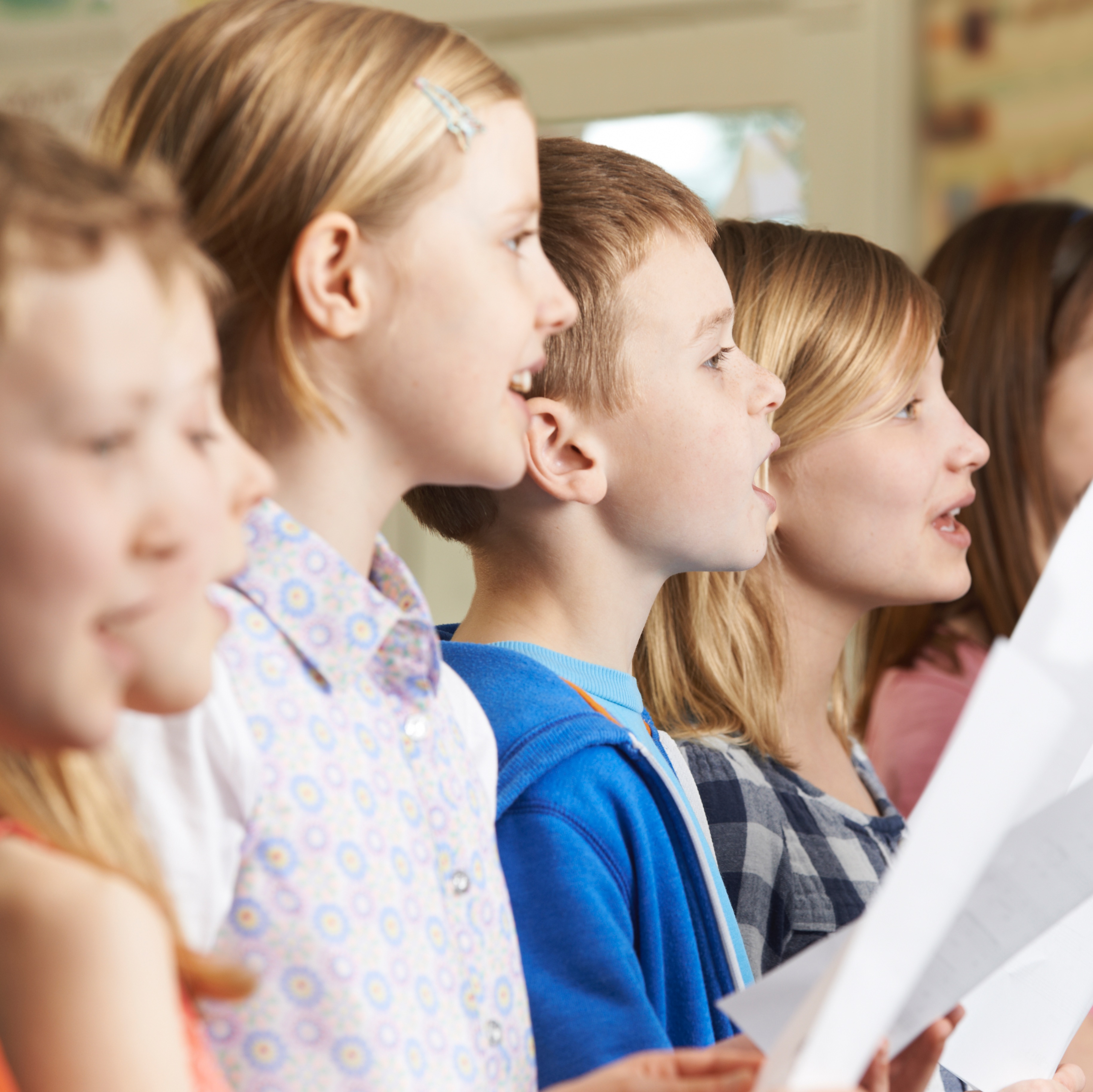 Kinder singen in einem Chor, halten Notenblätter und schauen nach rechts.