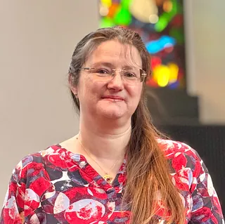 Lächelnde Frau mit langen braunen Haaren und Brille drinnen.